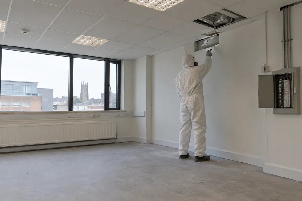 Protected surveyor in a vacant commercial room prepared for intrusive inspection
